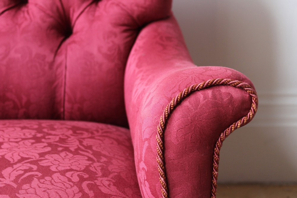A Victorian low armchair featuring red floral damask upholstery, deep button back detailing, scroll arms, and turned dark timber front legs on brass castors. View IV