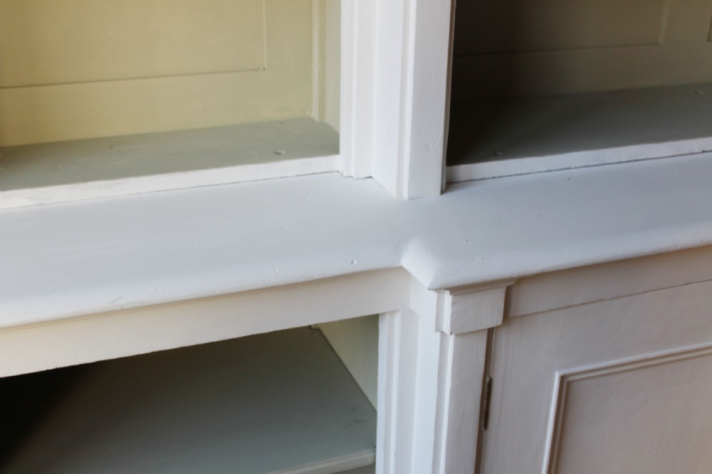 A large 19th-century painted breakfront bookcase featuring a central projecting section, open adjustable upper and lower side shelves, twin panelled lower cupboard doors, and a light grey interior backing. View III