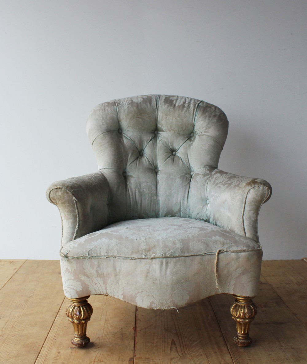 A 19th-century button-backed armchair upholstered in patterned pale sage damask fabric with rolled arms and turned gilded front legs.
