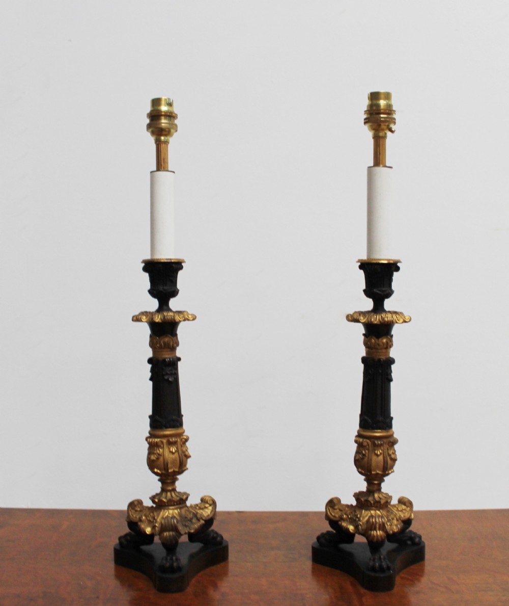 A pair of 19th-century style table lamps featuring black patinated columns with ornate gilt-bronze foliage accents and claw-footed bases.