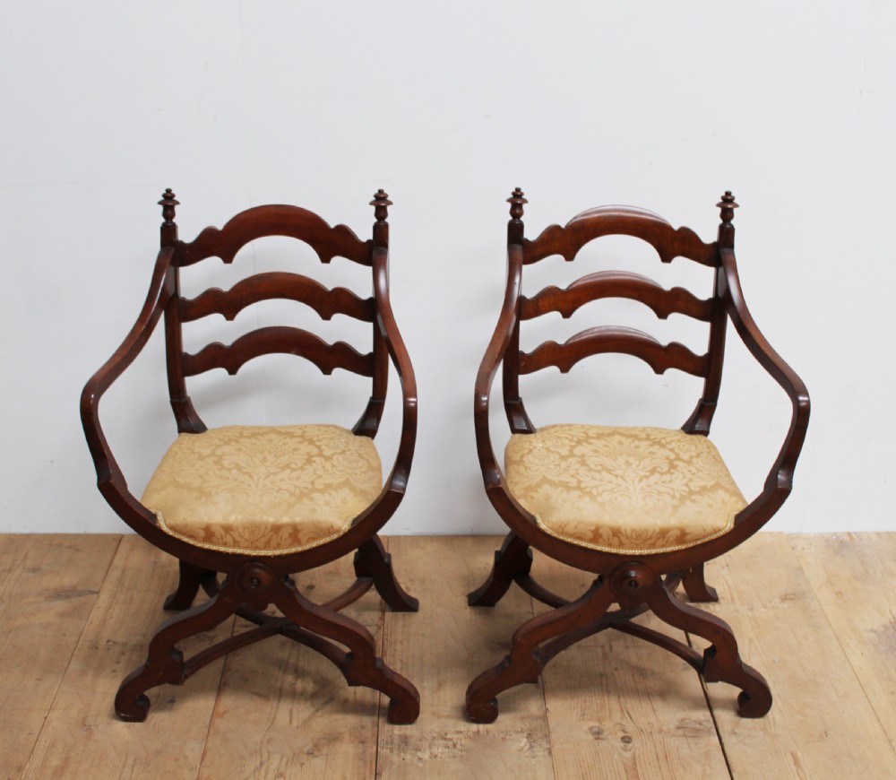 A pair of dark wood 19th-century X-frame armchairs featuring serpentine ladder-back splats, carved finials, and gold patterned fabric seats. View II