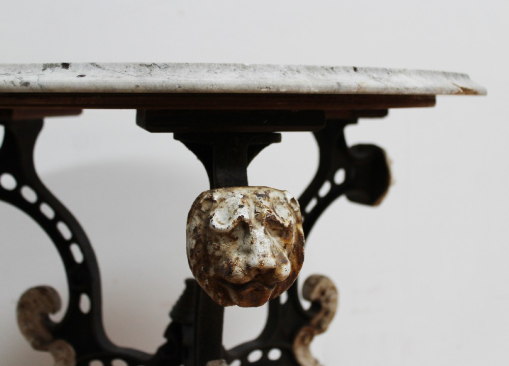 An antique nineteenth-century bistro table featuring a weathered circular marble top supported by a cast iron tripod base with lion mask details and claw feet. View II