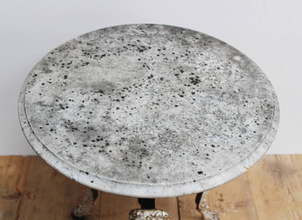 An antique nineteenth-century bistro table featuring a weathered circular marble top supported by a cast iron tripod base with lion mask details and claw feet. View III