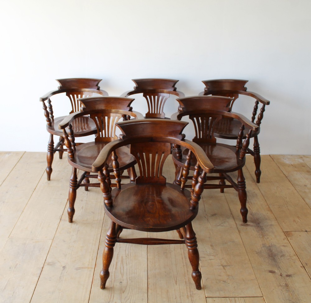 A set of six dark wooden captain armchairs featuring curved horseshoe backrests, slatted splats, and turned legs on a light timber floor.