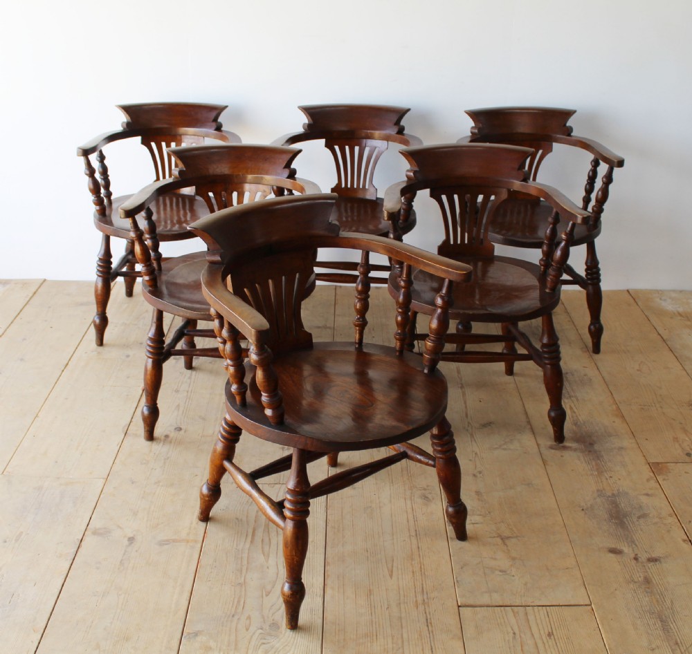 A set of six dark wooden captain armchairs featuring curved horseshoe backrests, slatted splats, and turned legs on a light timber floor. View II