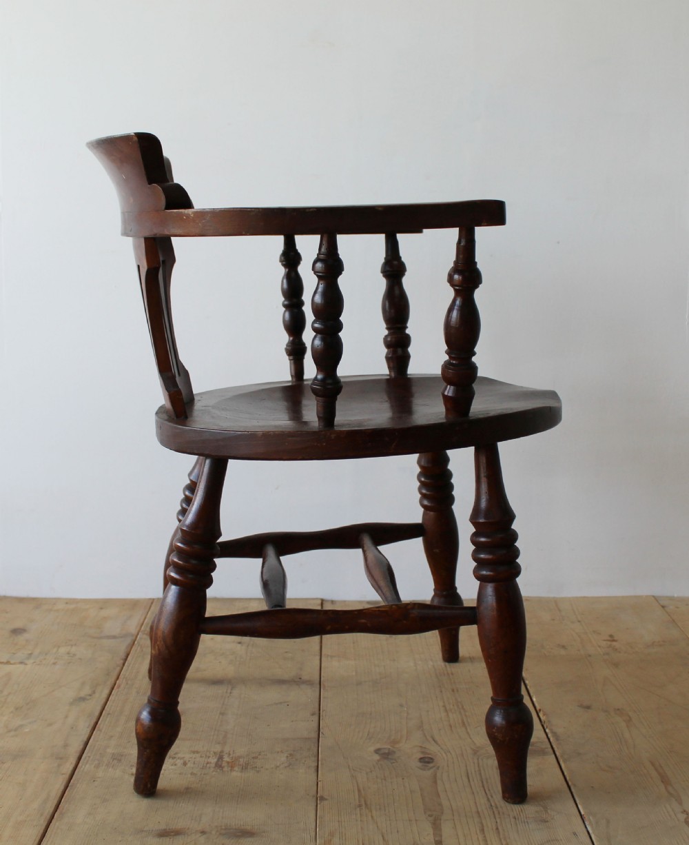 A set of six dark wooden captain armchairs featuring curved horseshoe backrests, slatted splats, and turned legs on a light timber floor. View III
