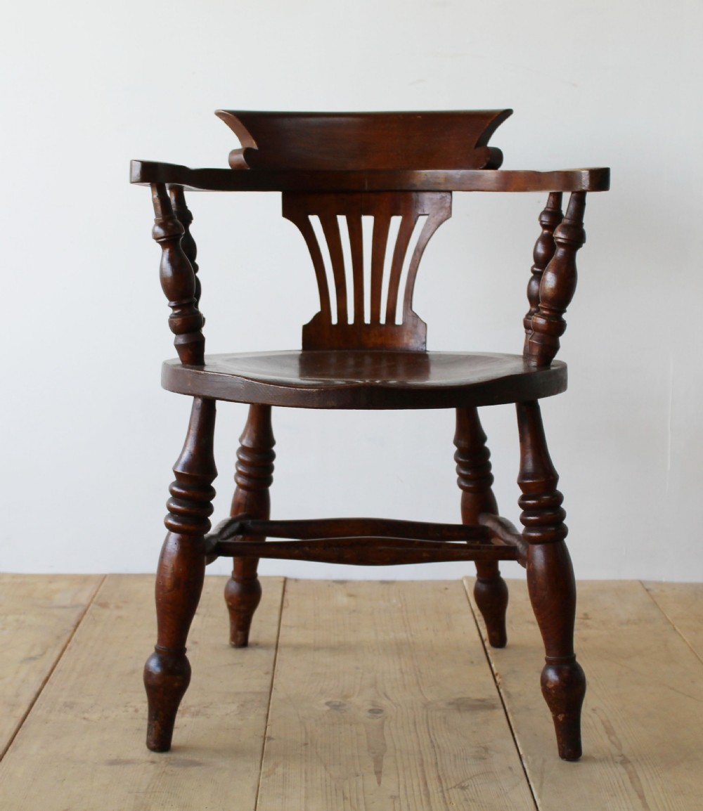 A set of six dark wooden captain armchairs featuring curved horseshoe backrests, slatted splats, and turned legs on a light timber floor. View V