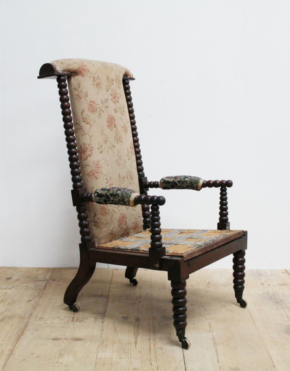 A 19th-century high-backed armchair featuring dark bobbin-turned wooden spindles, floral upholstery on the backrest, and brass castors on the legs.