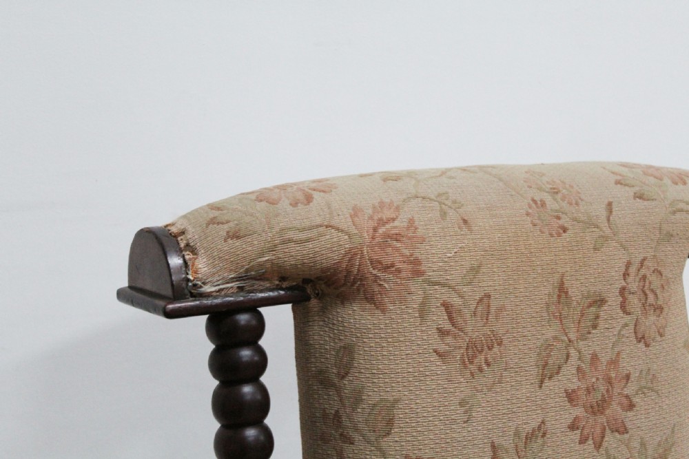 A 19th-century high-backed armchair featuring dark bobbin-turned wooden spindles, floral upholstery on the backrest, and brass castors on the legs. View II