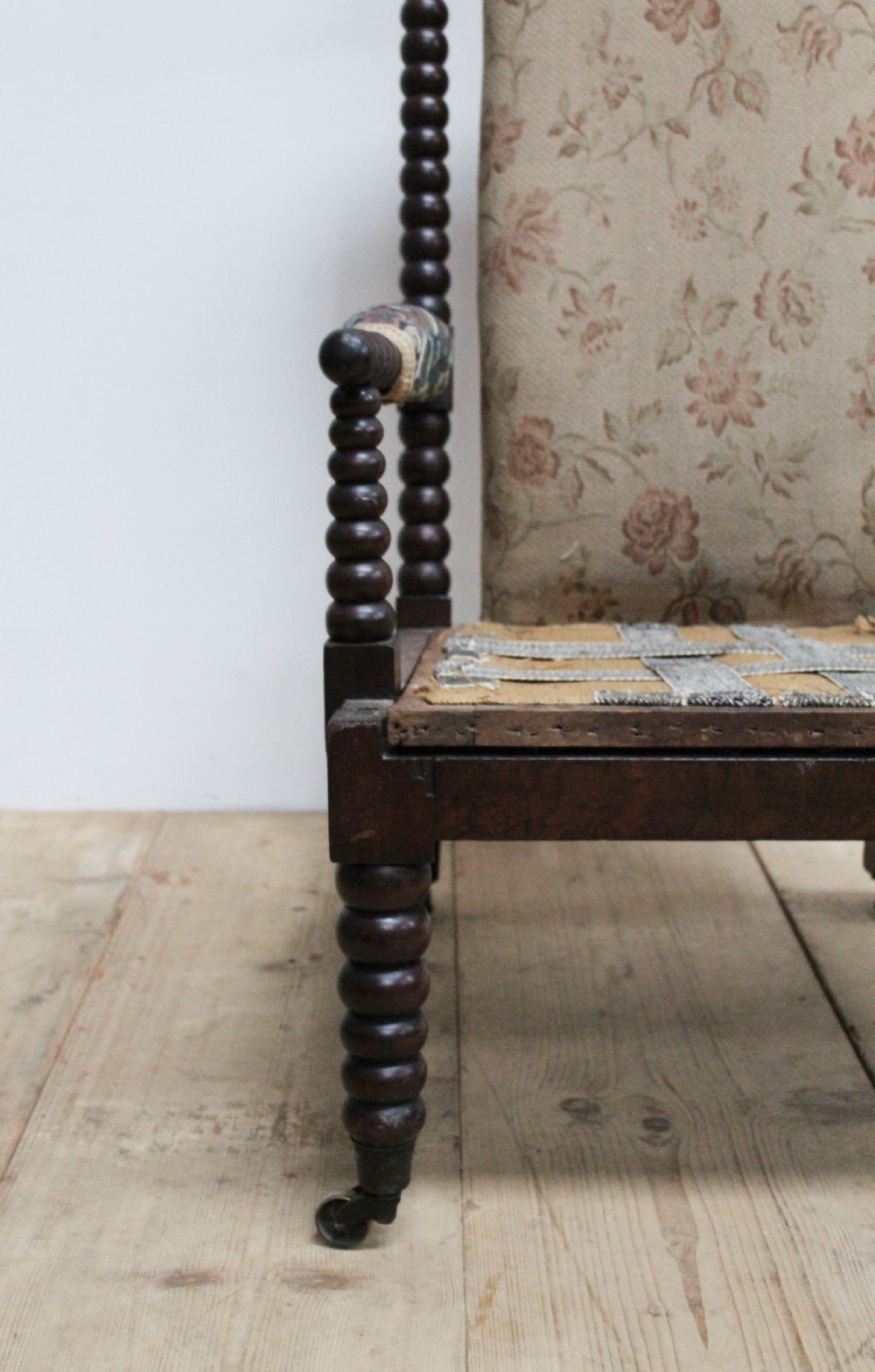 A 19th-century high-backed armchair featuring dark bobbin-turned wooden spindles, floral upholstery on the backrest, and brass castors on the legs. View III