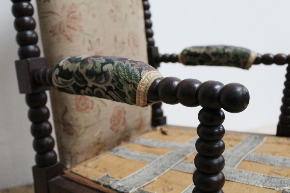 A 19th-century high-backed armchair featuring dark bobbin-turned wooden spindles, floral upholstery on the backrest, and brass castors on the legs. View IV