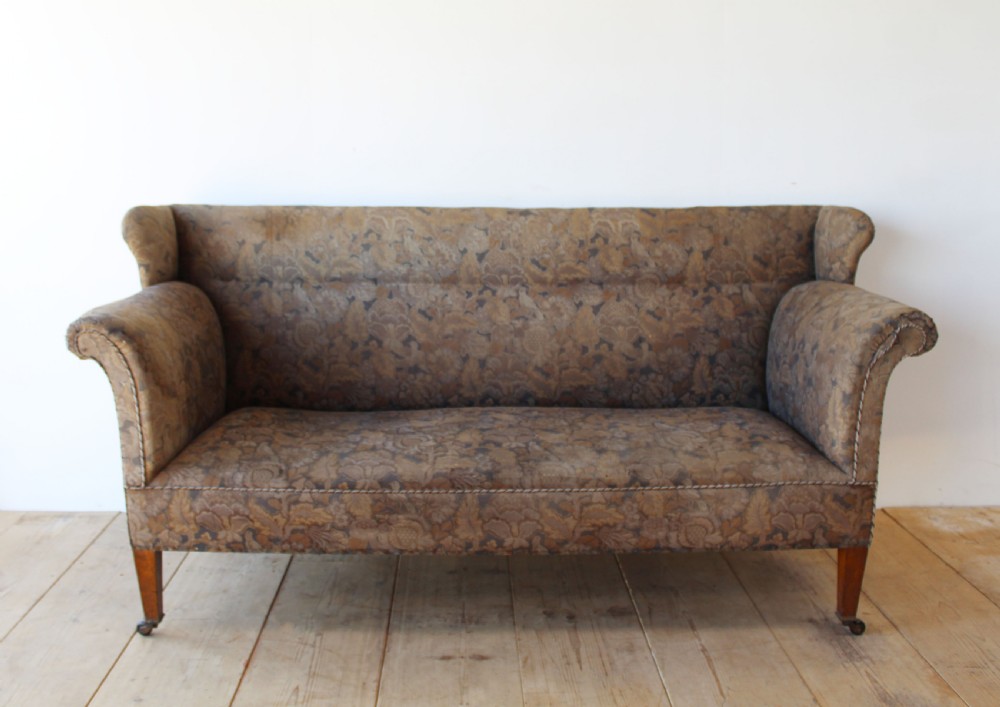 A nineteenth-century upholstered sofa featuring brown patterned tapestry fabric, scrolled arms, a high back, and tapered timber legs with brass castors.