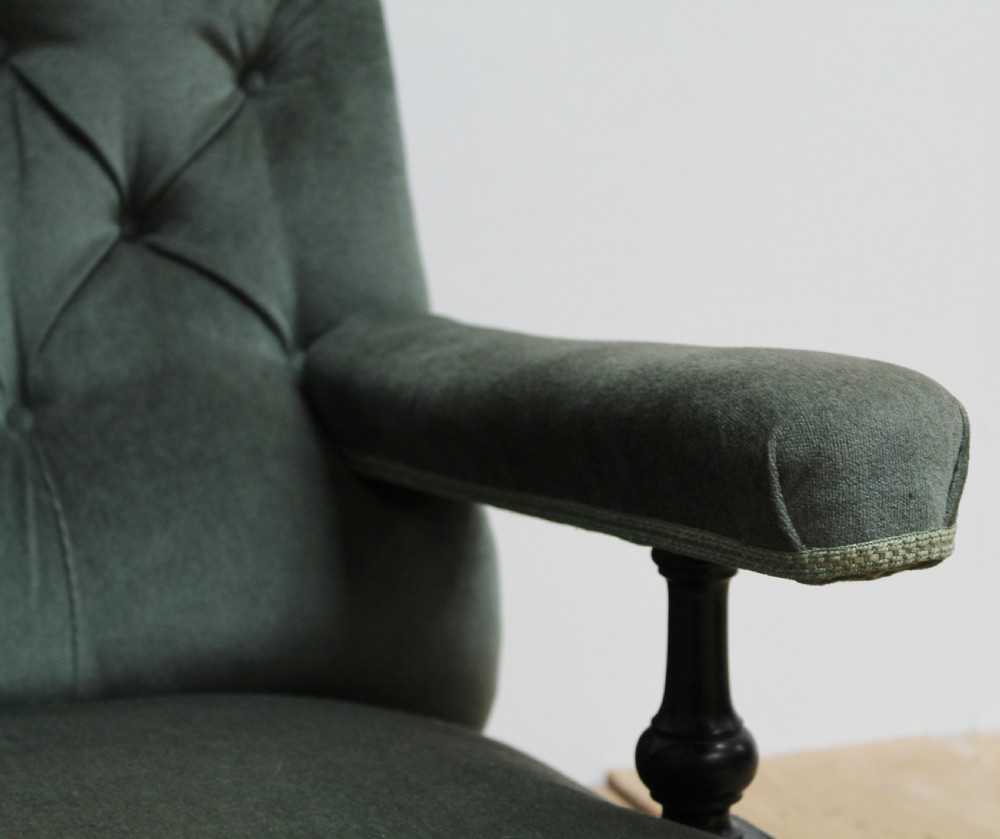 A low-slung Howard style armchair upholstered in sage green velvet featuring deep buttoning on the backrest and turned wooden legs on castors. View II