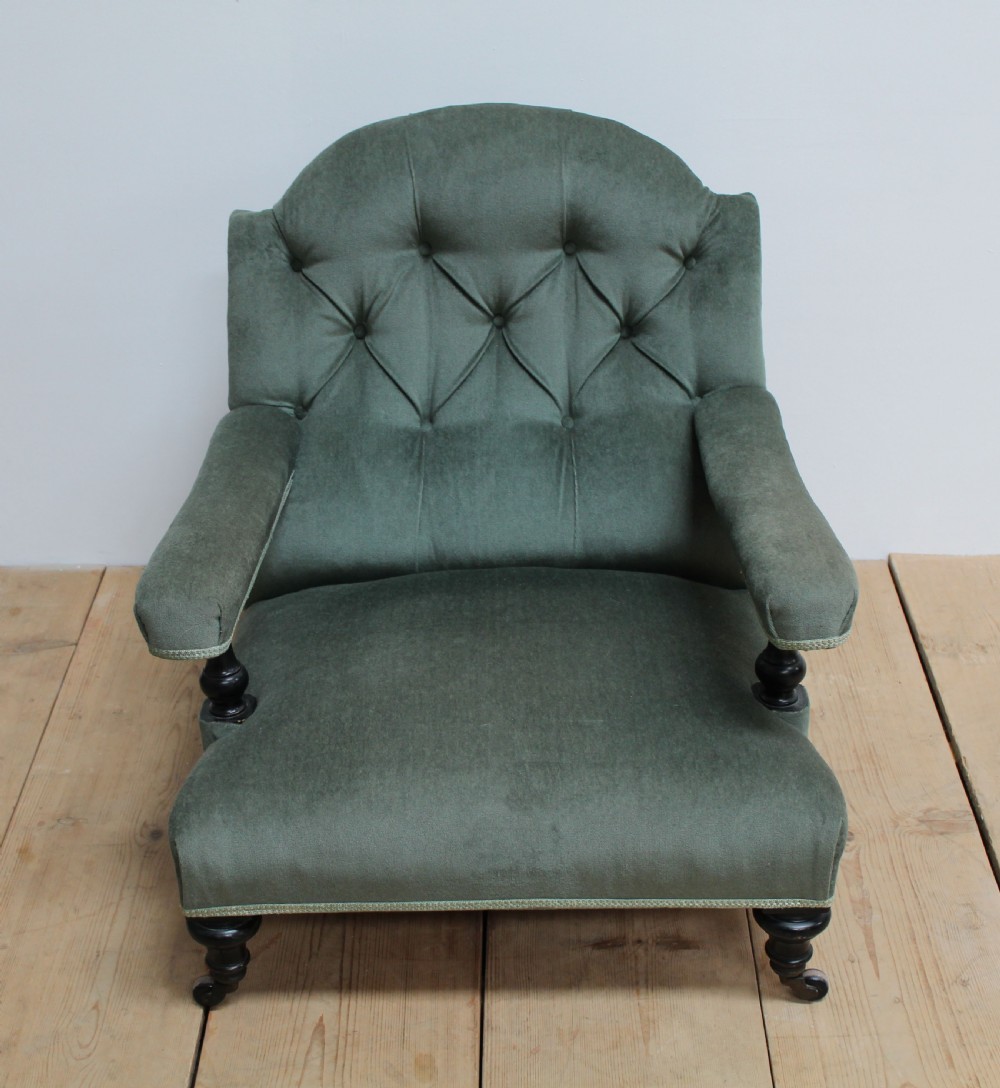 A low-slung Howard style armchair upholstered in sage green velvet featuring deep buttoning on the backrest and turned wooden legs on castors. View III