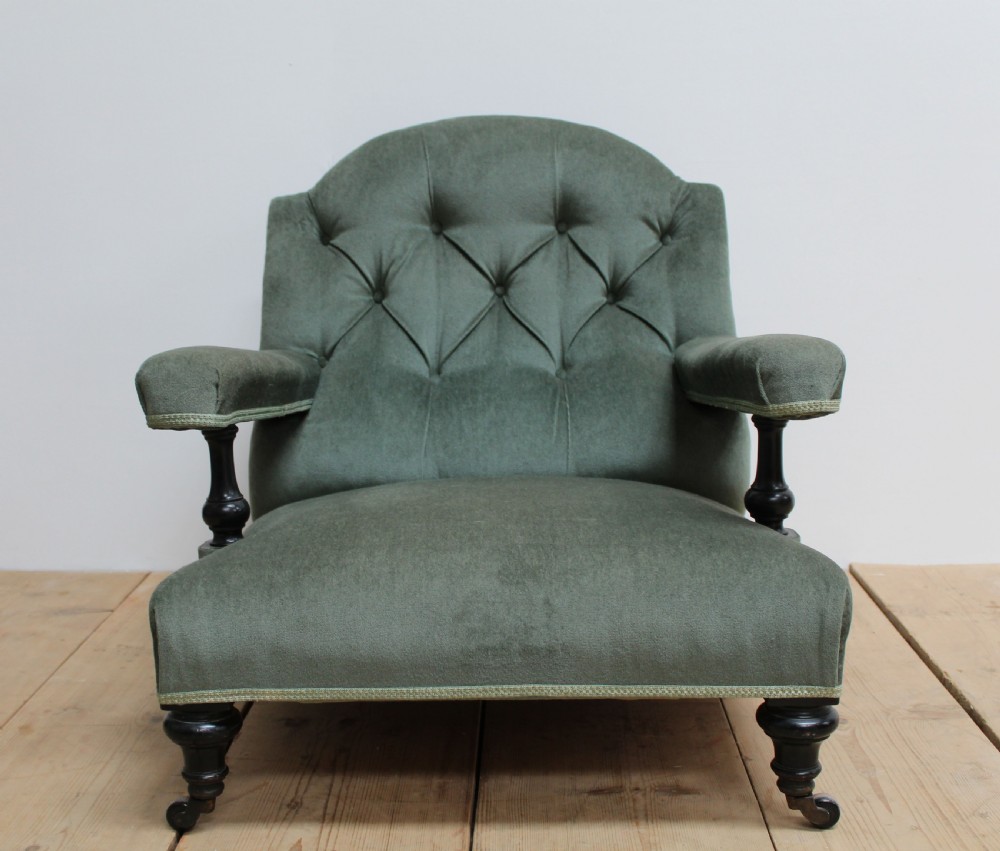 A low-slung Howard style armchair upholstered in sage green velvet featuring deep buttoning on the backrest and turned wooden legs on castors. View IV