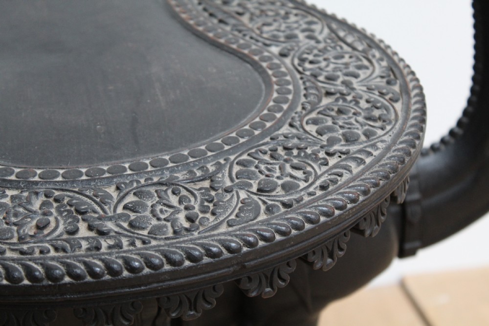 A dark carved wooden side table crafted in the form of a standing camel supporting a circular carved top on its saddle base. View IV