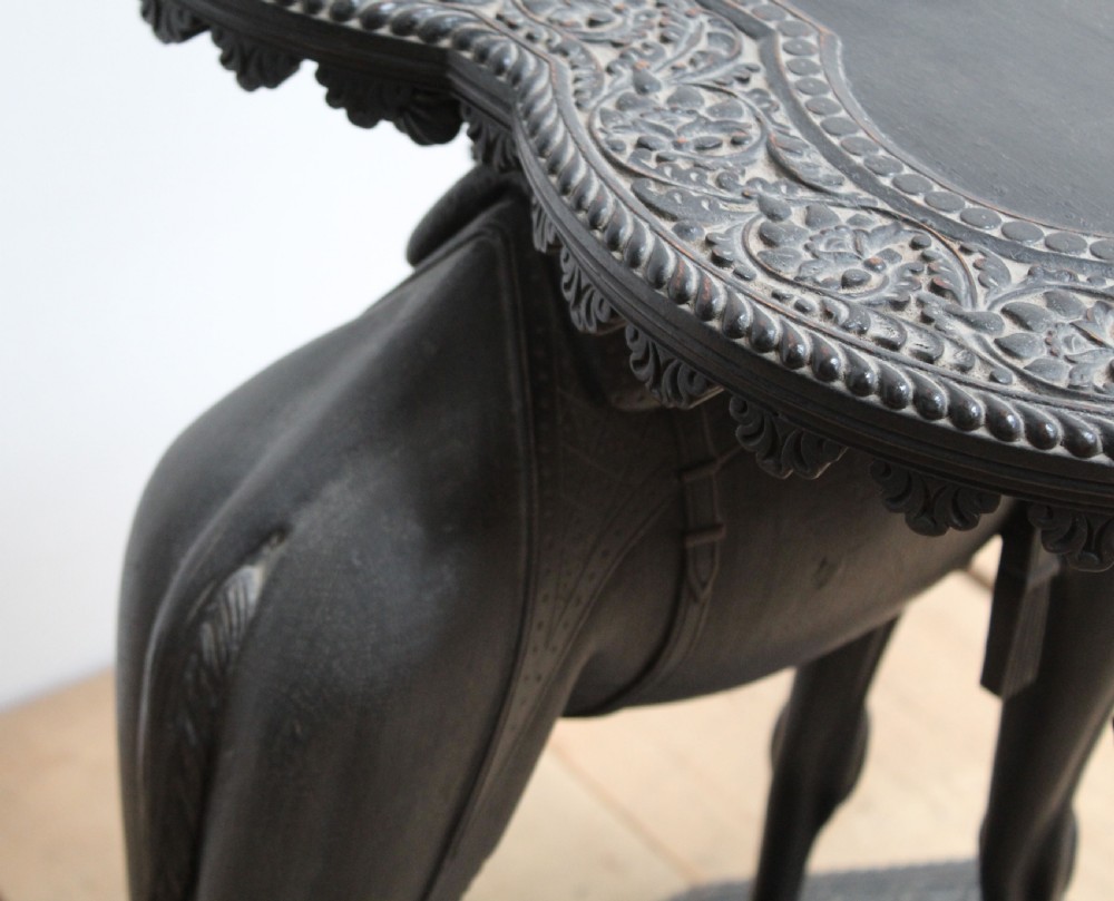 A dark carved wooden side table crafted in the form of a standing camel supporting a circular carved top on its saddle base. View VI