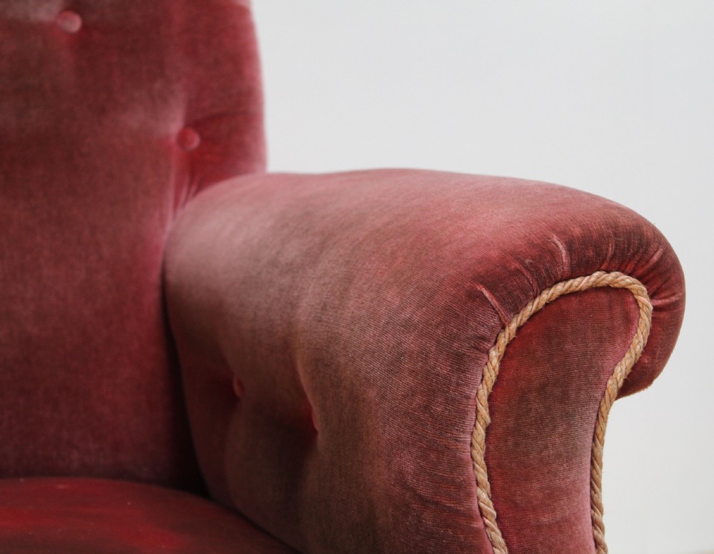 A Victorian armchair upholstered in faded red velvet featuring a button-backed backrest, rolled arms, and turned wooden front legs on brass castors. View II