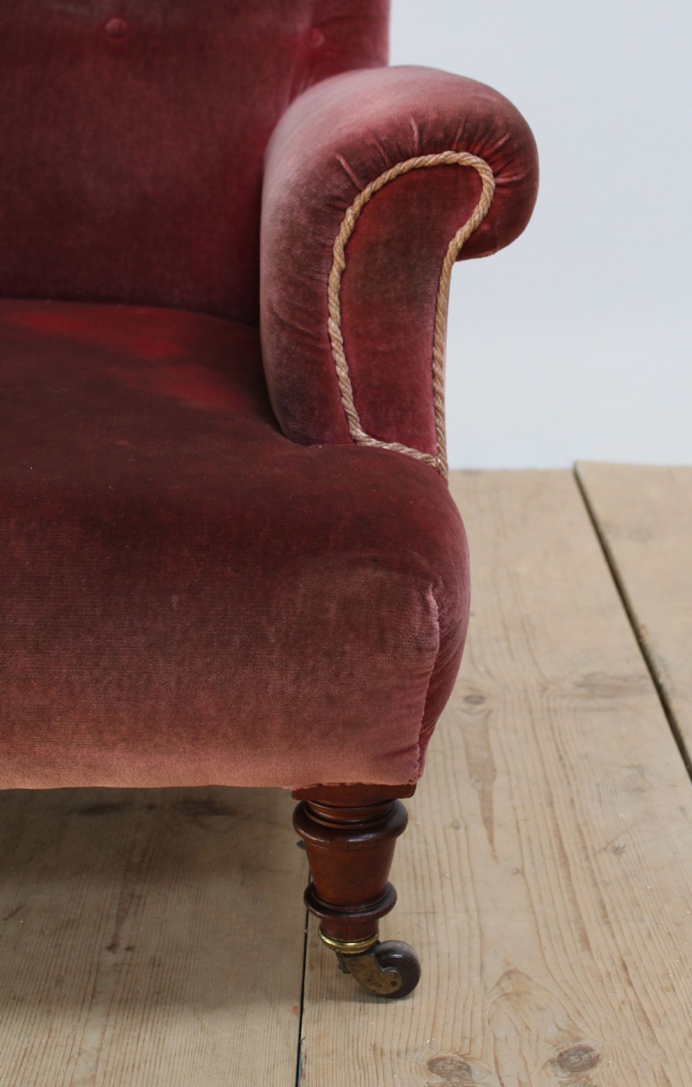 A Victorian armchair upholstered in faded red velvet featuring a button-backed backrest, rolled arms, and turned wooden front legs on brass castors. View III