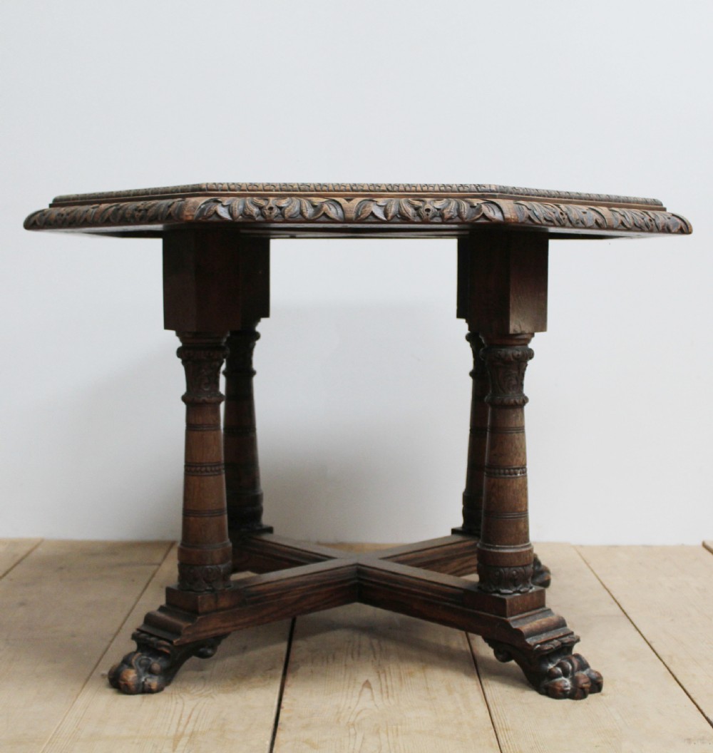 A 19th-century octagonal dark oak centre table with a carved foliate apron, turned columnar legs, an X-shaped stretcher, and carved paw feet.