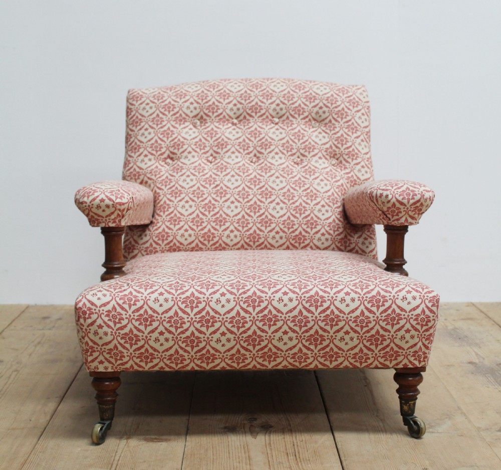 A low-seated Victorian upholstered armchair with patterned red and cream fabric, turned wooden arm supports, and brass castors.