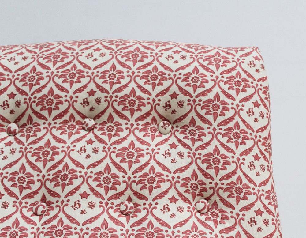 A low-seated Victorian upholstered armchair with patterned red and cream fabric, turned wooden arm supports, and brass castors. View V