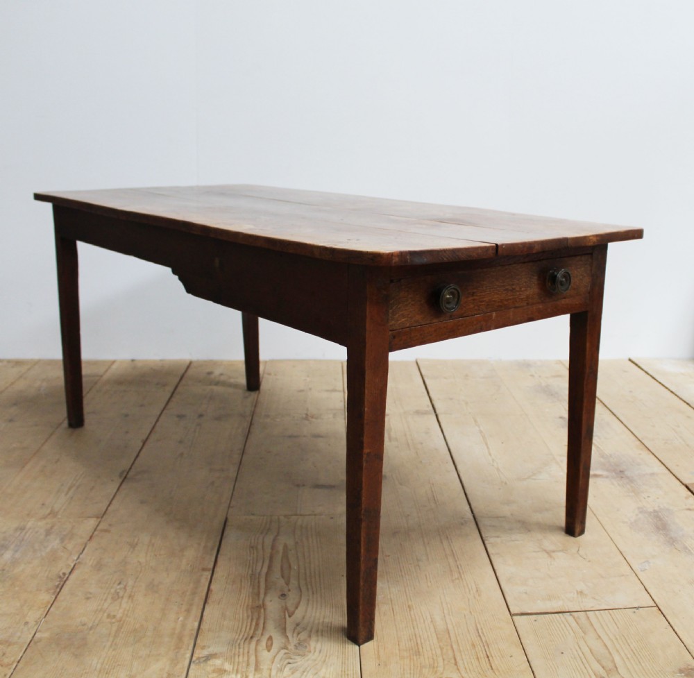 A 19th-century rustic wooden farmhouse dining table featuring a planked top, tapered square legs, and a single end drawer with wooden knobs.