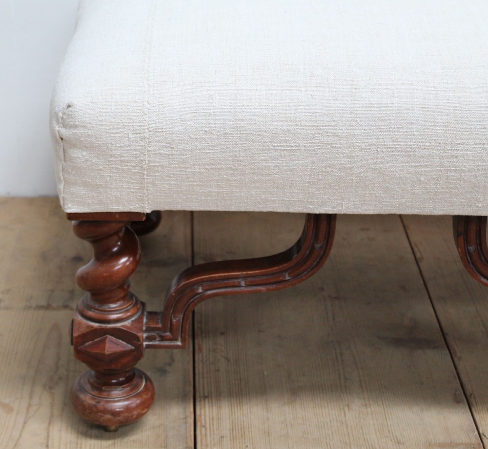 A low 19th-century footstool featuring cream linen upholstery, four carved barley twist legs, shaped stretchers, and brass castors. View II
