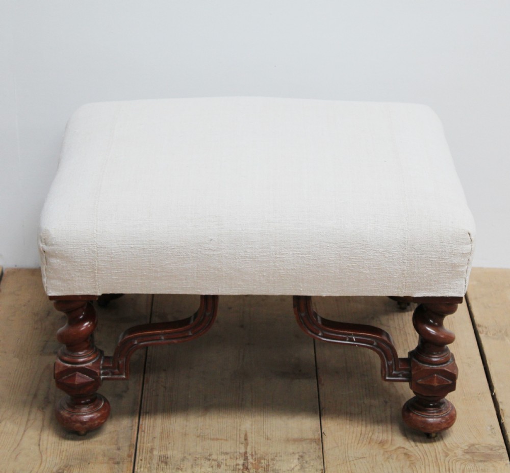 A low 19th-century footstool featuring cream linen upholstery, four carved barley twist legs, shaped stretchers, and brass castors. View III