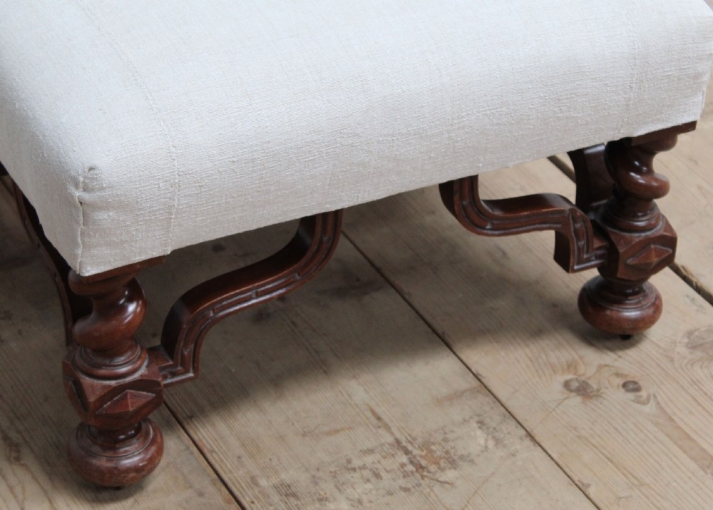 A low 19th-century footstool featuring cream linen upholstery, four carved barley twist legs, shaped stretchers, and brass castors. View IV