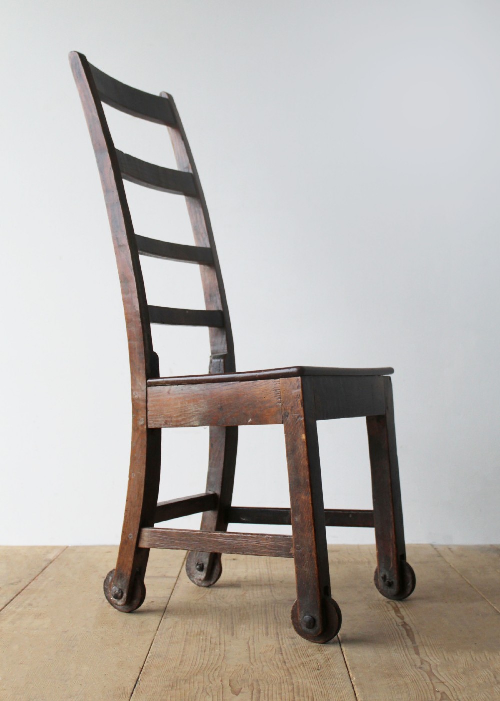 A 19th-century dark wood ladder-back side chair resting on four wooden wheels.