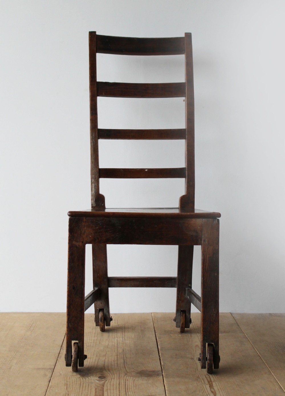 A 19th-century dark wood ladder-back side chair resting on four wooden wheels. View II