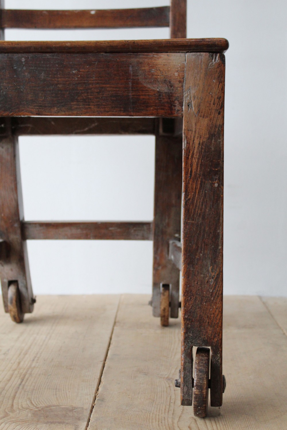 A 19th-century dark wood ladder-back side chair resting on four wooden wheels. View IV