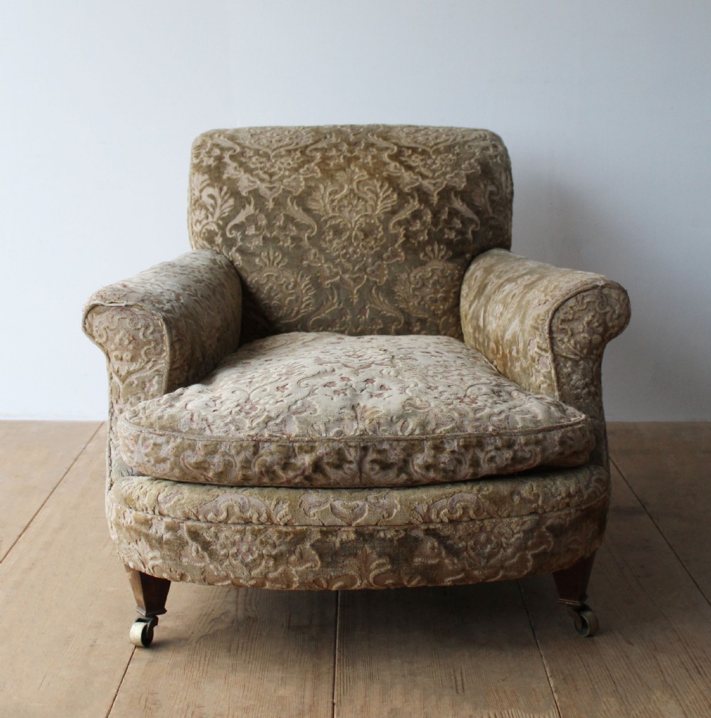 An Edwardian Howard style club chair upholstered in patterned olive green velvet featuring rolled arms and short legs on brass castors.