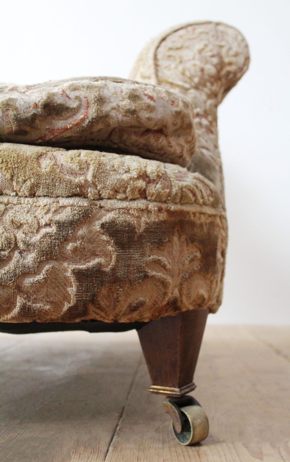 An Edwardian Howard style club chair upholstered in patterned olive green velvet featuring rolled arms and short legs on brass castors. View II