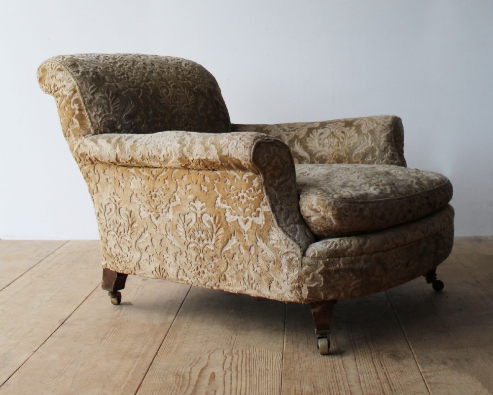 An Edwardian Howard style club chair upholstered in patterned olive green velvet featuring rolled arms and short legs on brass castors. View III