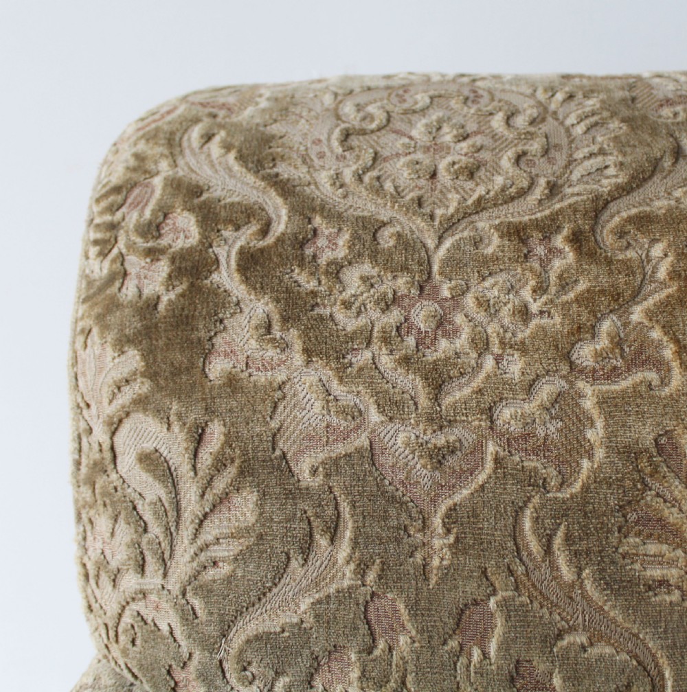 An Edwardian Howard style club chair upholstered in patterned olive green velvet featuring rolled arms and short legs on brass castors. View IV
