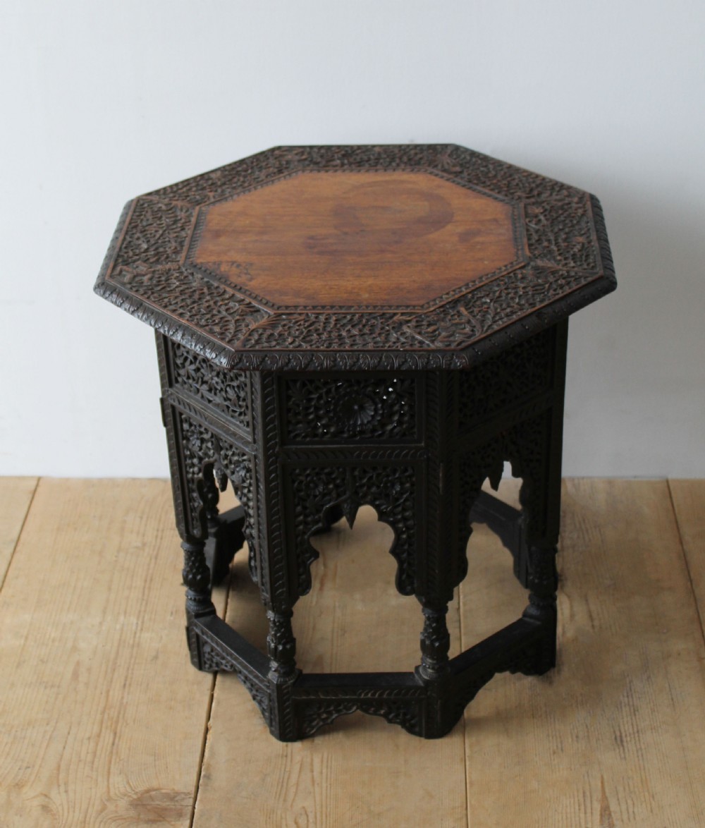 An octagonal dark hardwood side table featuring intricate openwork fretwork carving along the base and geometric borders surrounding a smooth central top.