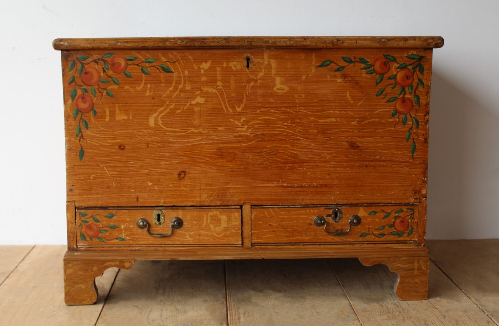 A 19th-century pine mule chest featuring two lower drawers, brass handles, bracket feet, and hand-painted fruit and leaf motifs on the front corners.