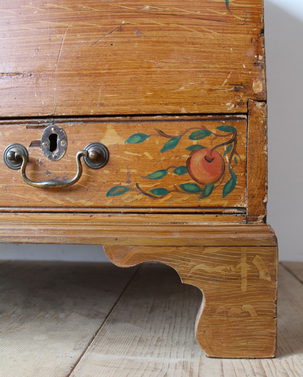 A 19th-century pine mule chest featuring two lower drawers, brass handles, bracket feet, and hand-painted fruit and leaf motifs on the front corners. View III