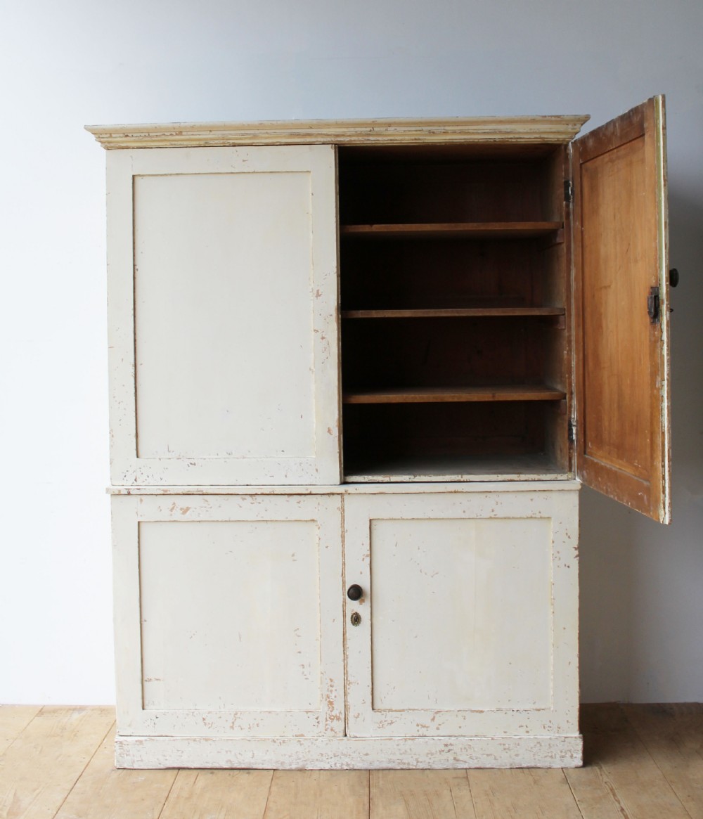 A tall 19th-century two-tier painted wooden linen cupboard with four panelled doors, a distressed off-white finish, turned wooden knobs, and brass keyhole escutcheons. View II