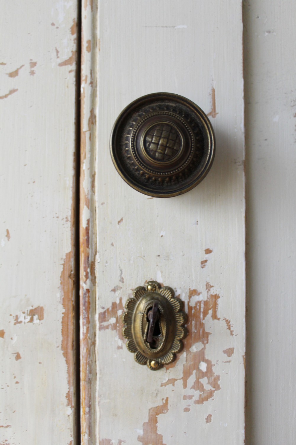 A tall 19th-century two-tier painted wooden linen cupboard with four panelled doors, a distressed off-white finish, turned wooden knobs, and brass keyhole escutcheons. View IV
