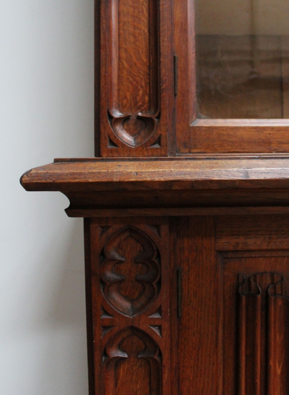An Early Victorian Gothic Revival oak two-tier bookcase featuring double glazed upper doors with traceried arches and lower cupboard doors with carved linenfold panels. View II