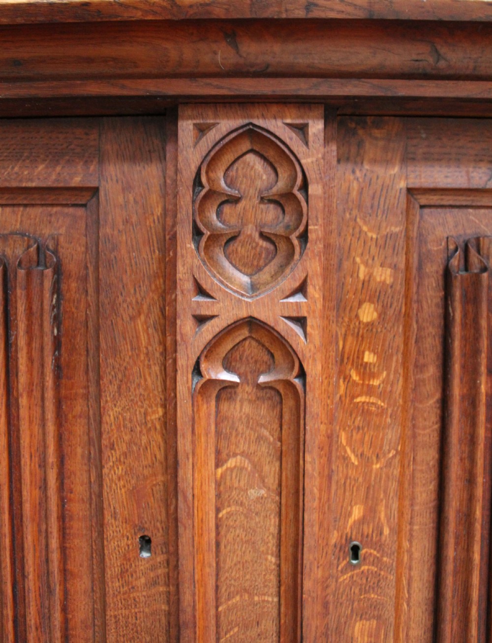 An Early Victorian Gothic Revival oak two-tier bookcase featuring double glazed upper doors with traceried arches and lower cupboard doors with carved linenfold panels. View III