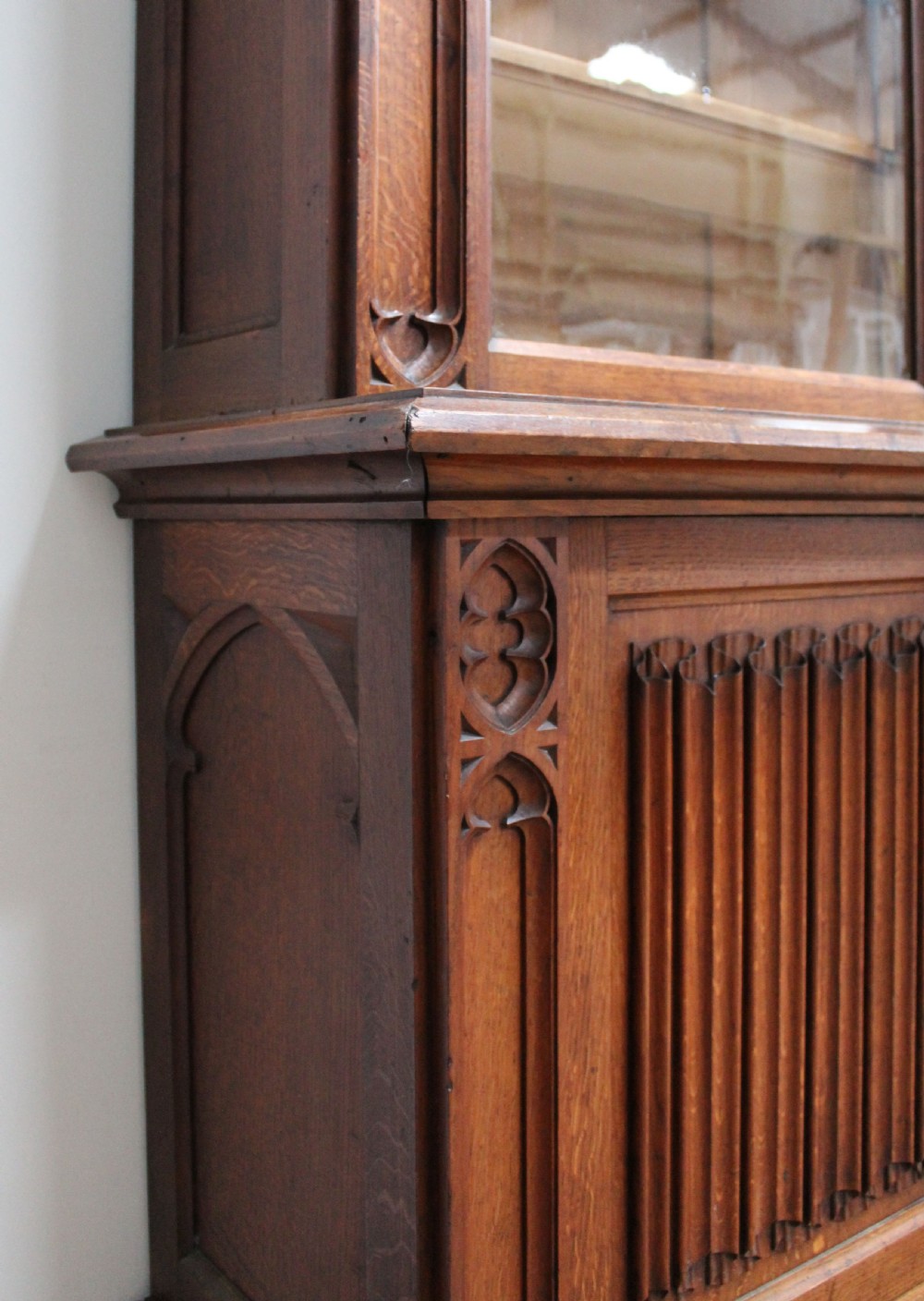 An Early Victorian Gothic Revival oak two-tier bookcase featuring double glazed upper doors with traceried arches and lower cupboard doors with carved linenfold panels. View IV