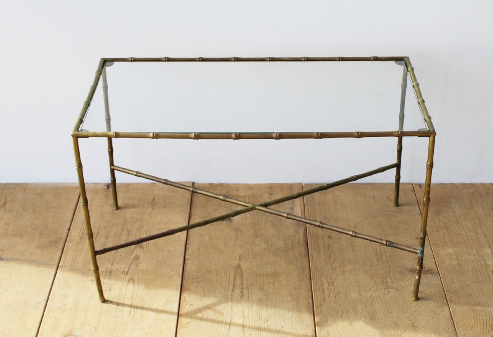 A rectangular coffee table featuring an aged brass frame designed with faux bamboo nodes, an X-shaped cross-stretcher, and a clear glass top.