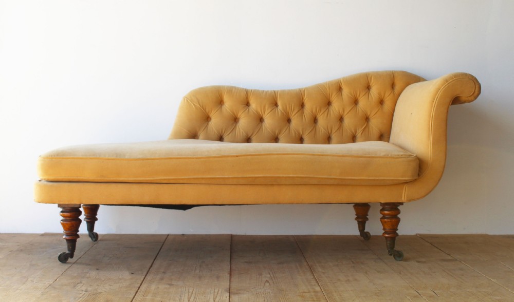 An early nineteenth-century chaise longue upholstered in mustard yellow velvet featuring deep-buttoned tufting, a scrolled arm, and turned wooden legs on castors.