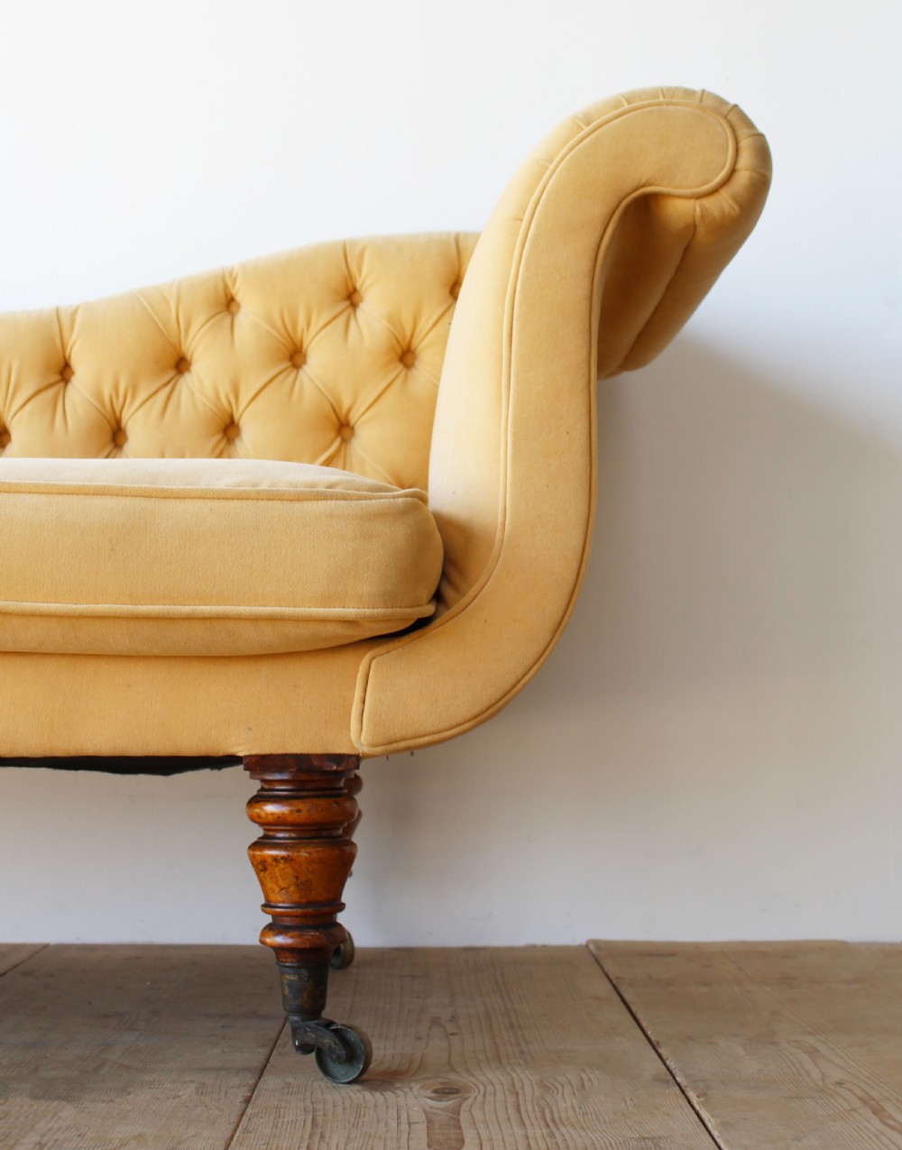 An early nineteenth-century chaise longue upholstered in mustard yellow velvet featuring deep-buttoned tufting, a scrolled arm, and turned wooden legs on castors. View II