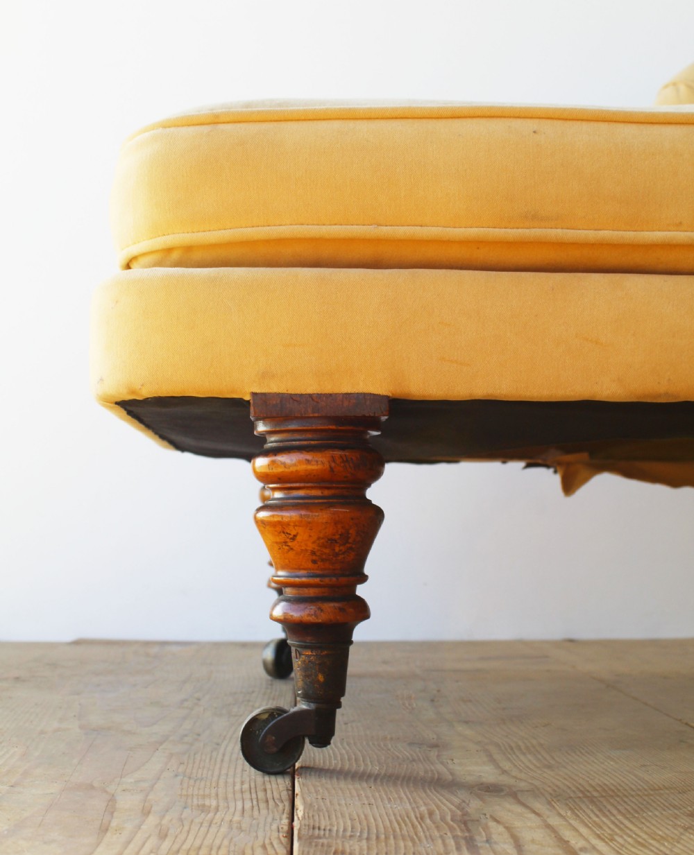 An early nineteenth-century chaise longue upholstered in mustard yellow velvet featuring deep-buttoned tufting, a scrolled arm, and turned wooden legs on castors. View IV