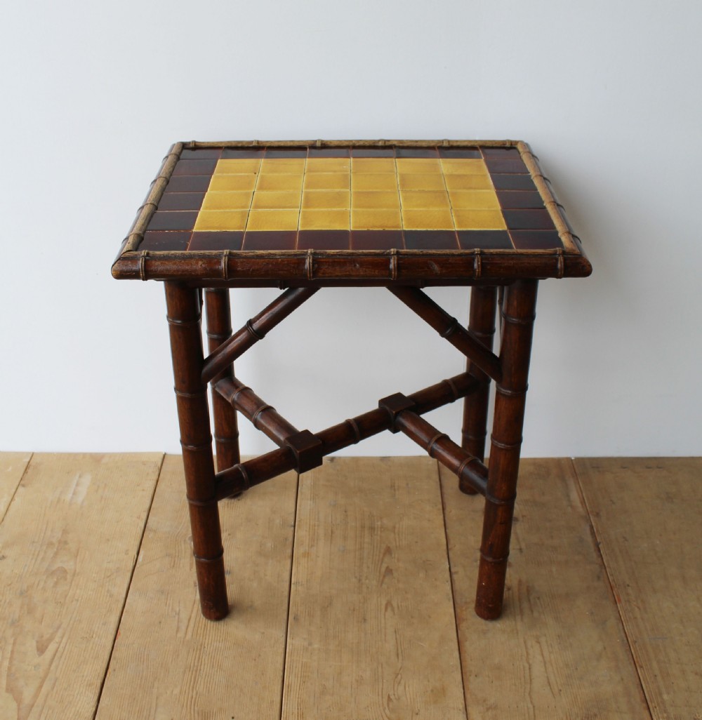 A late 19th-century dark bamboo lamp table featuring a square inset top lined with yellow and dark brown ceramic tiles and cross-braced legs.